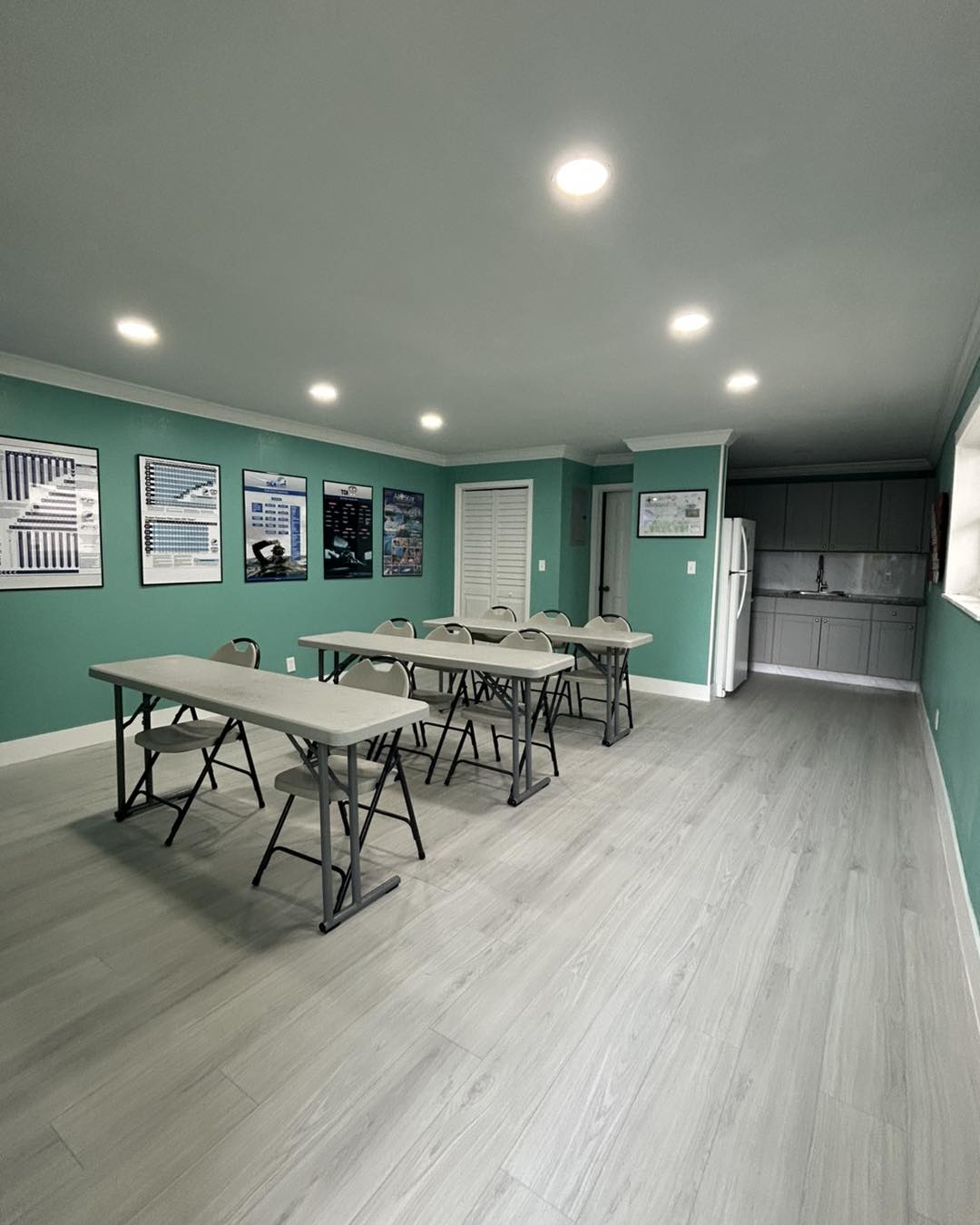 Room with teal walls, gray tables, and chairs on a light wood floor.