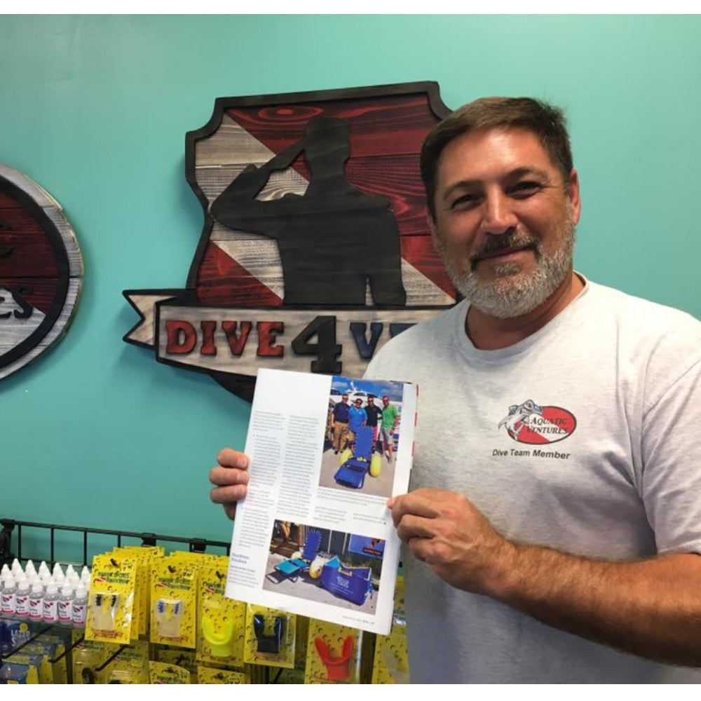 Man holding a document in front of a 'Dive 4' sign on a teal wall.
