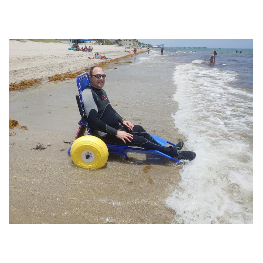 Person using a beach wheelchair on a sandy beach with ocean waves.