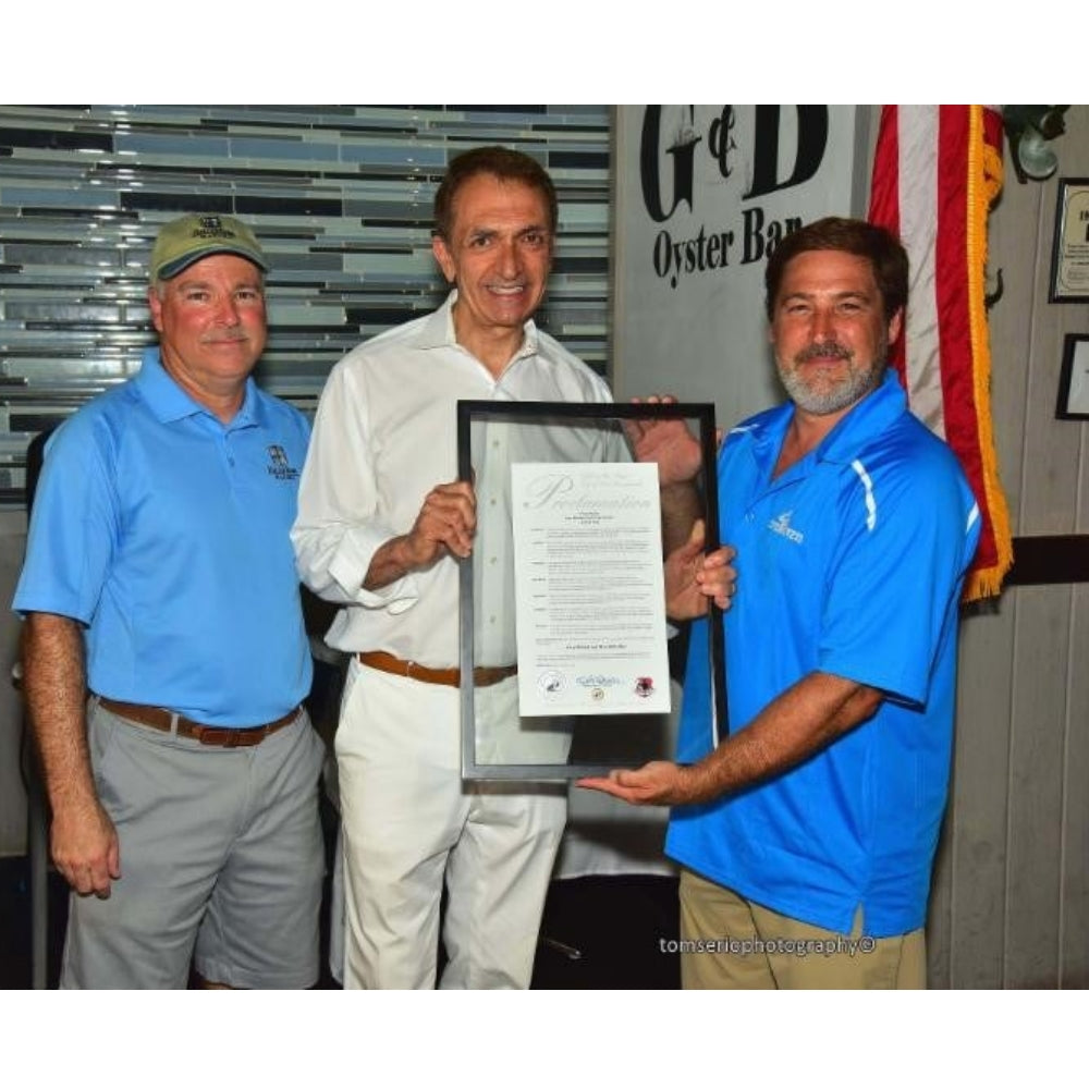 Three men holding a framed document in an indoor setting with a banner in the background.