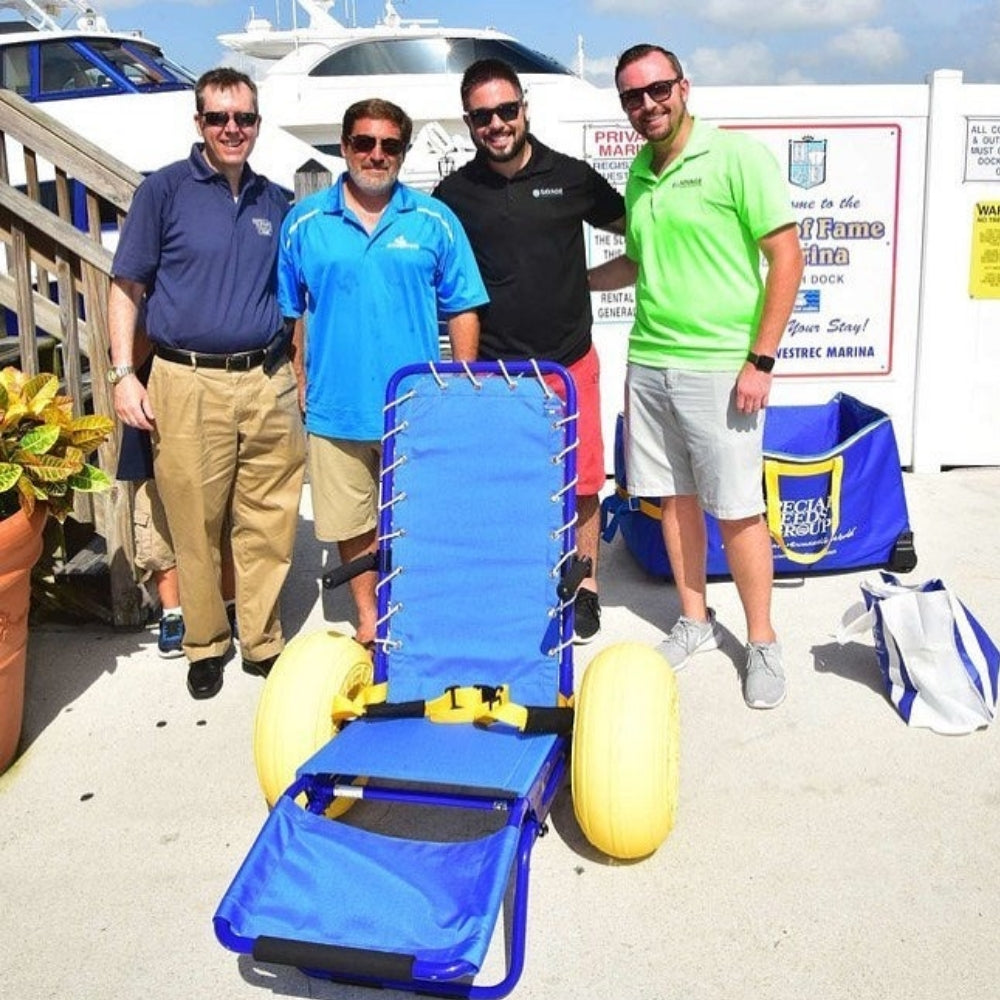 Four men standing next to a blue and yellow beach chair on a dock with boats in the background.